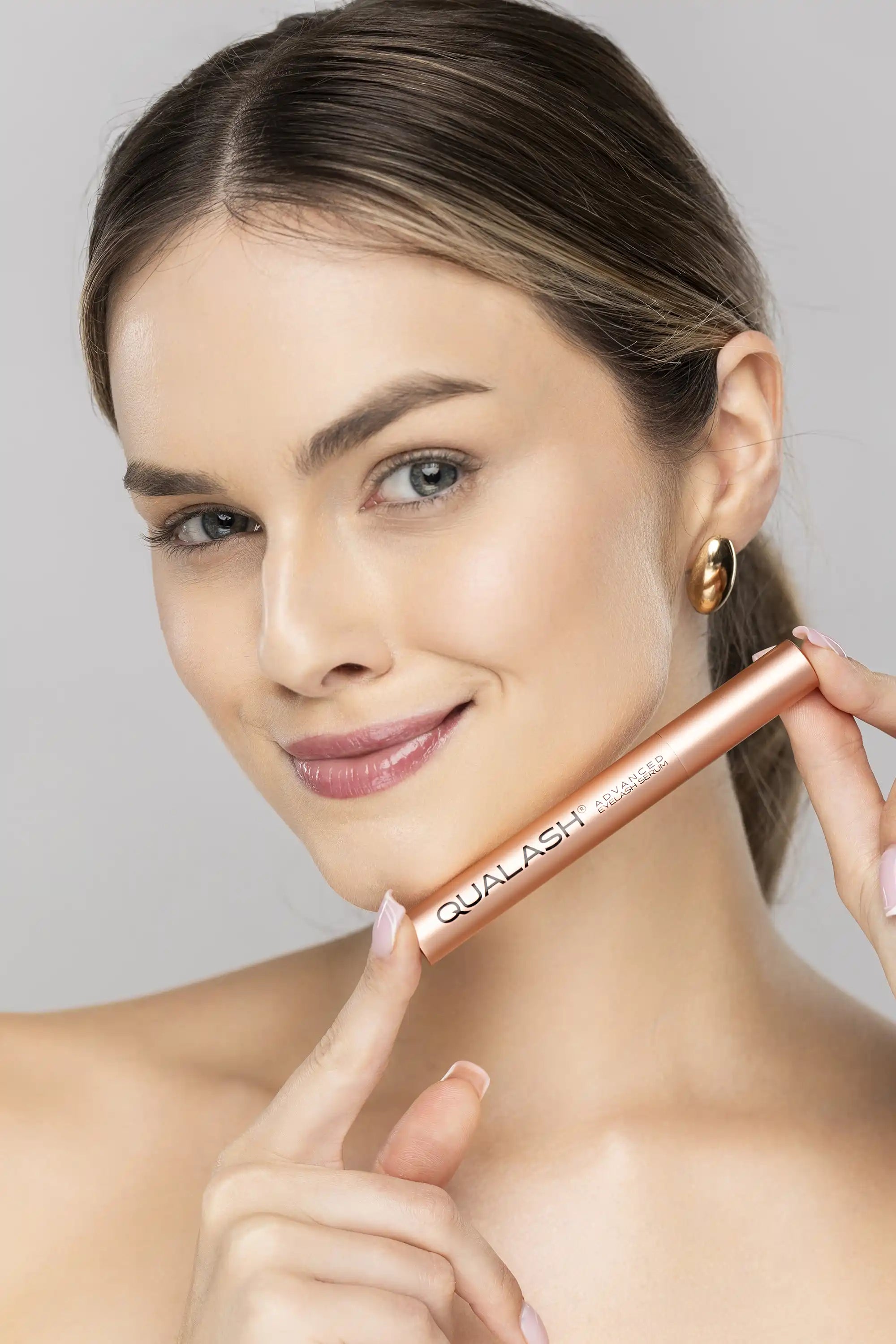 Smilende kvinde, der holder QUALASH Advanced Eyelash Serum inden påføring